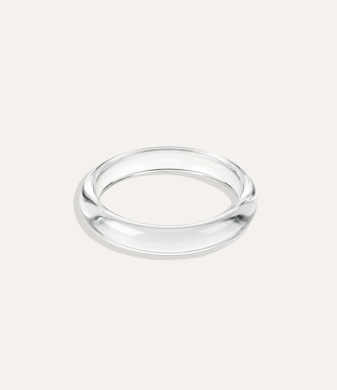 Close-up of a polished clear round bangle with a smooth, minimalist design on a neutral background.