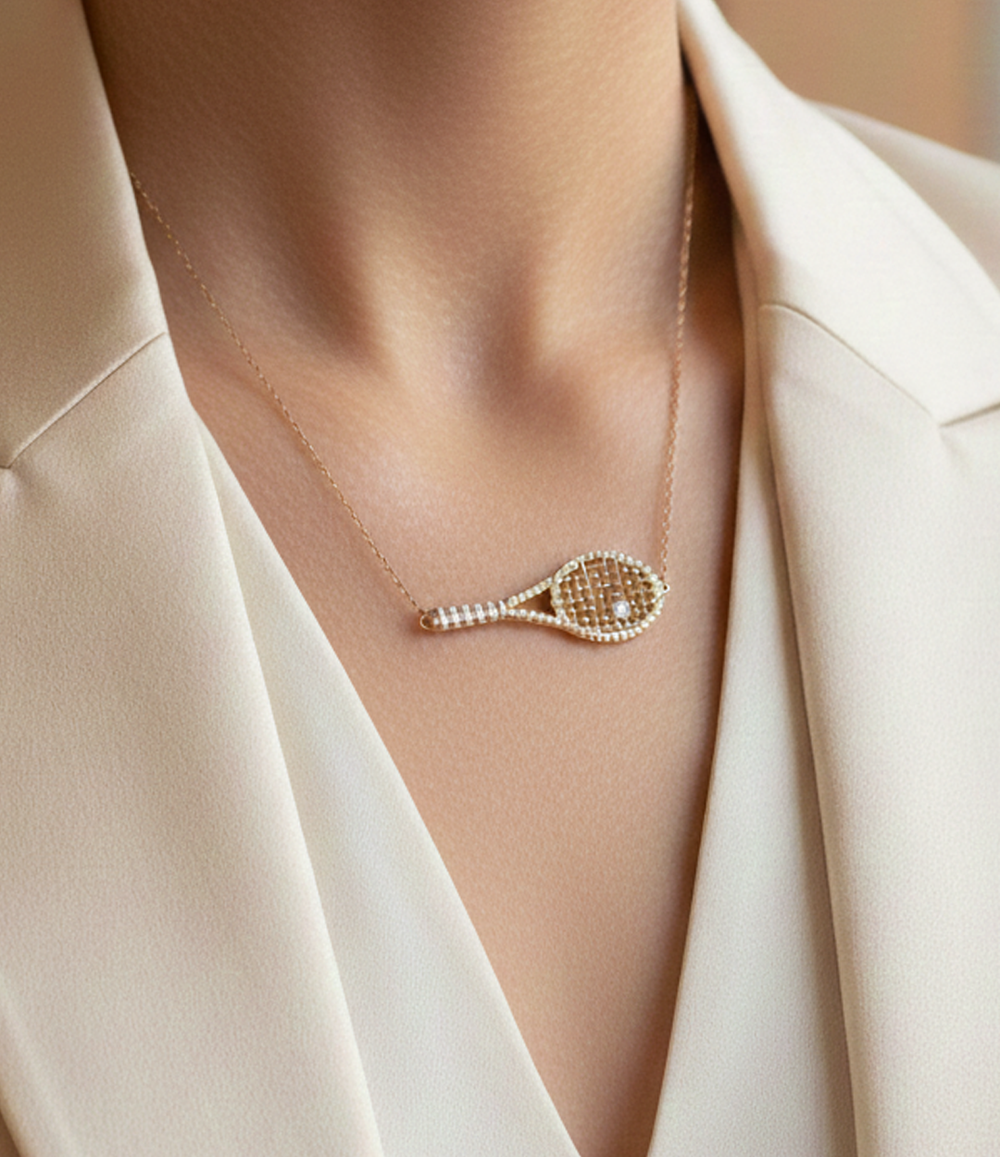 Necklace with a tennis racket pendant on a person wearing a beige outfit.