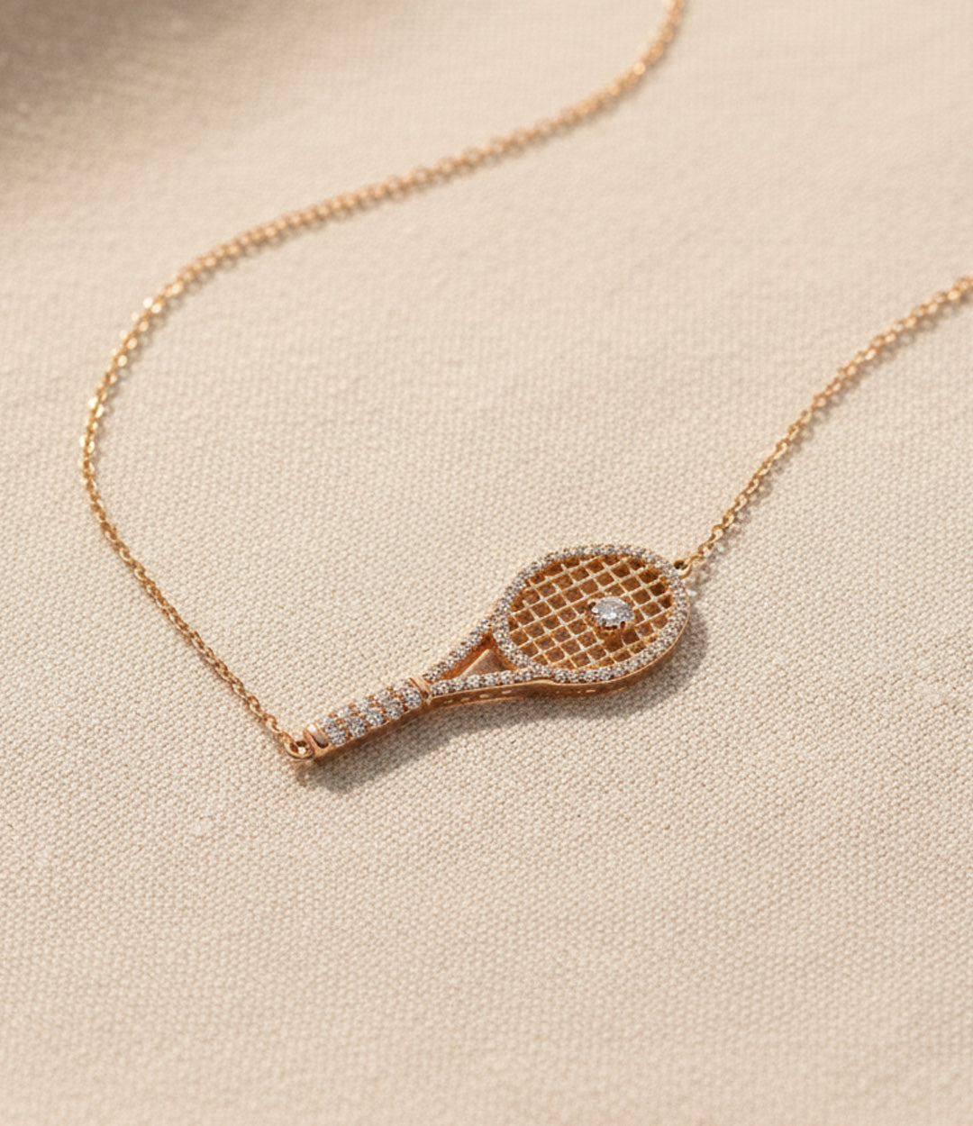 Rose gold tennis racket necklace with diamond details on a beige background