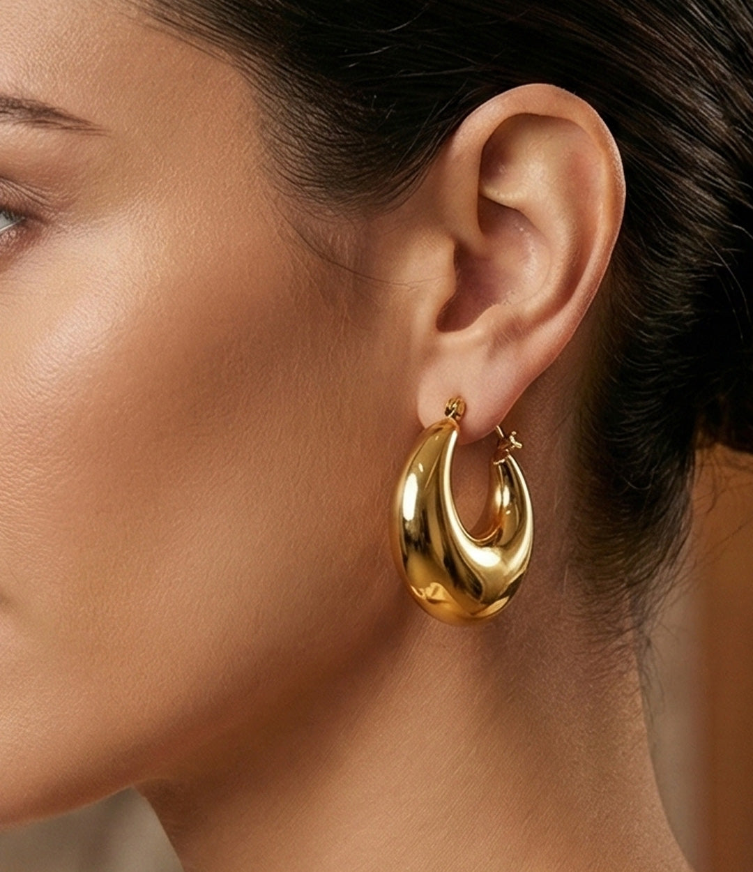 Gold hoop earring worn by a person with a neutral background