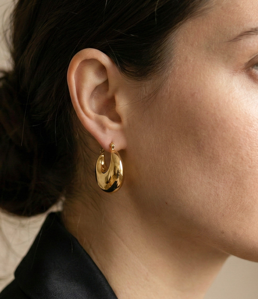 Close-up of a person wearing gold hoop earrings with a neutral background