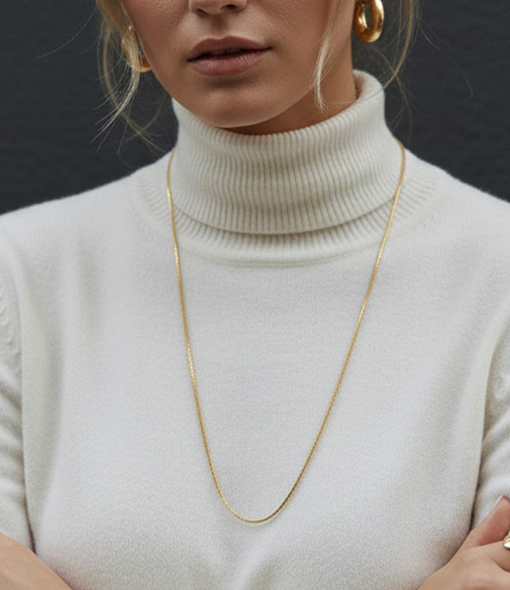 Person wearing a gold necklace with a plain background