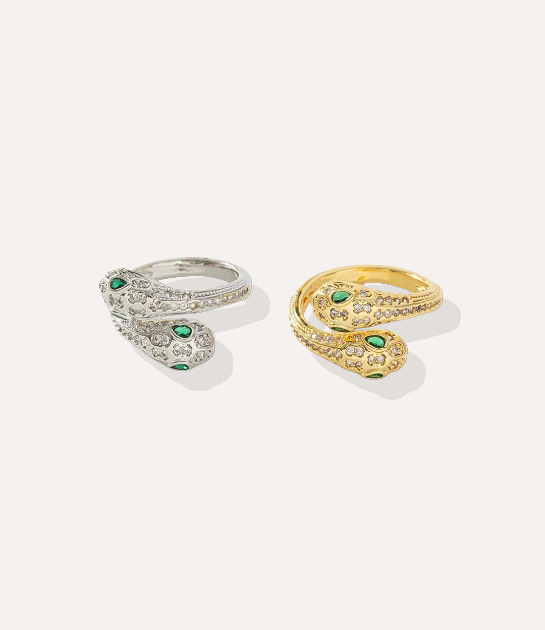 Two snake-shaped rings, one gold and one silver, with green gemstones on a light gray background.