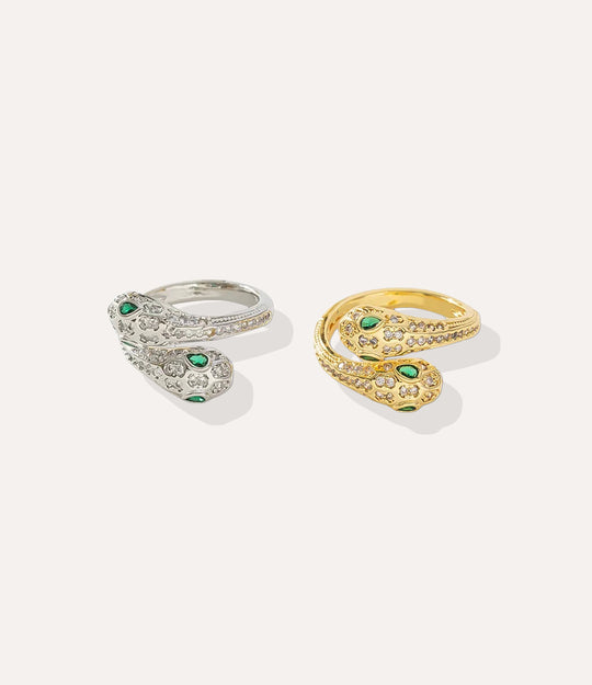 Two snake-shaped rings, one gold and one silver, with green gemstones on a light gray background.
