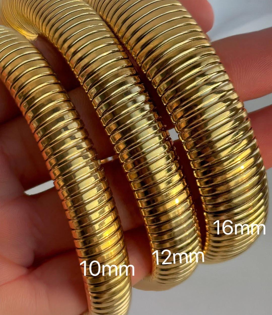 Gold bangles of different sizes held by a hand with measurements indicated.
