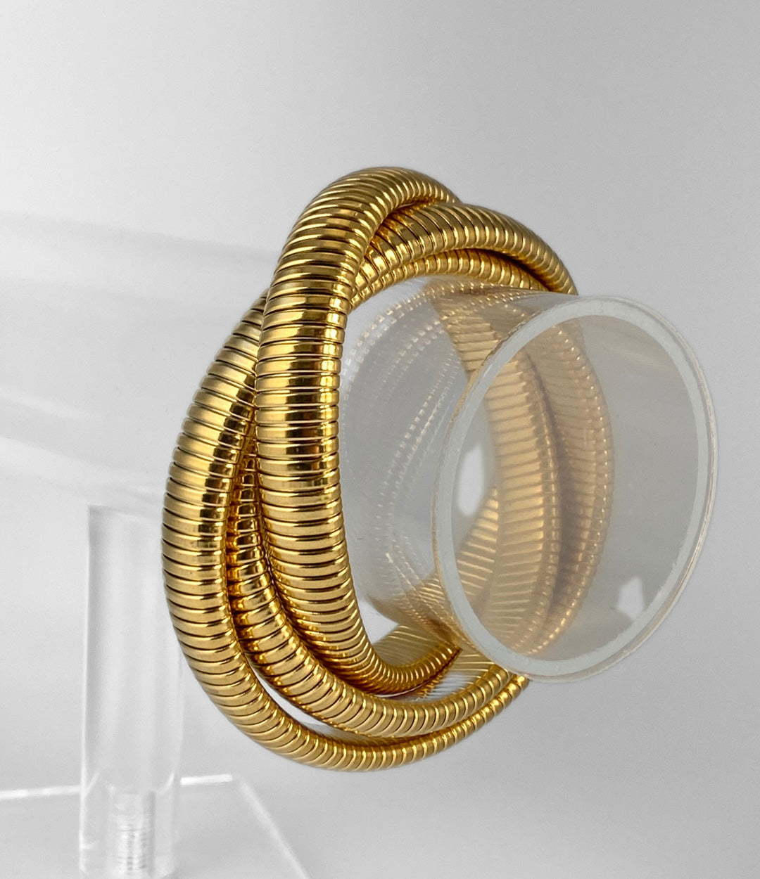 Gold bracelet on a clear stand against a white background