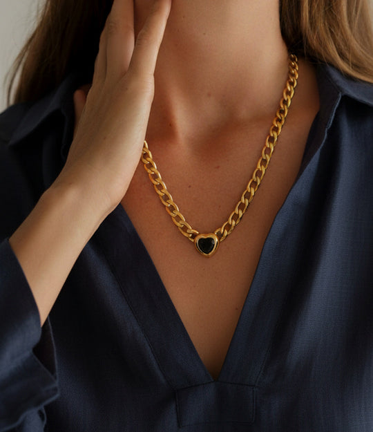 Gold chain necklace with a heart-shaped pendant worn by a person in a dark blue shirt.