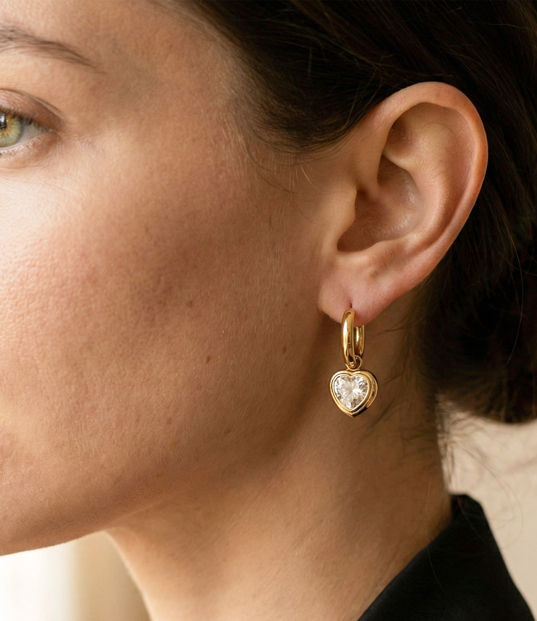 Close-up of a person wearing a gold heart-shaped earring with a clear gemstone.