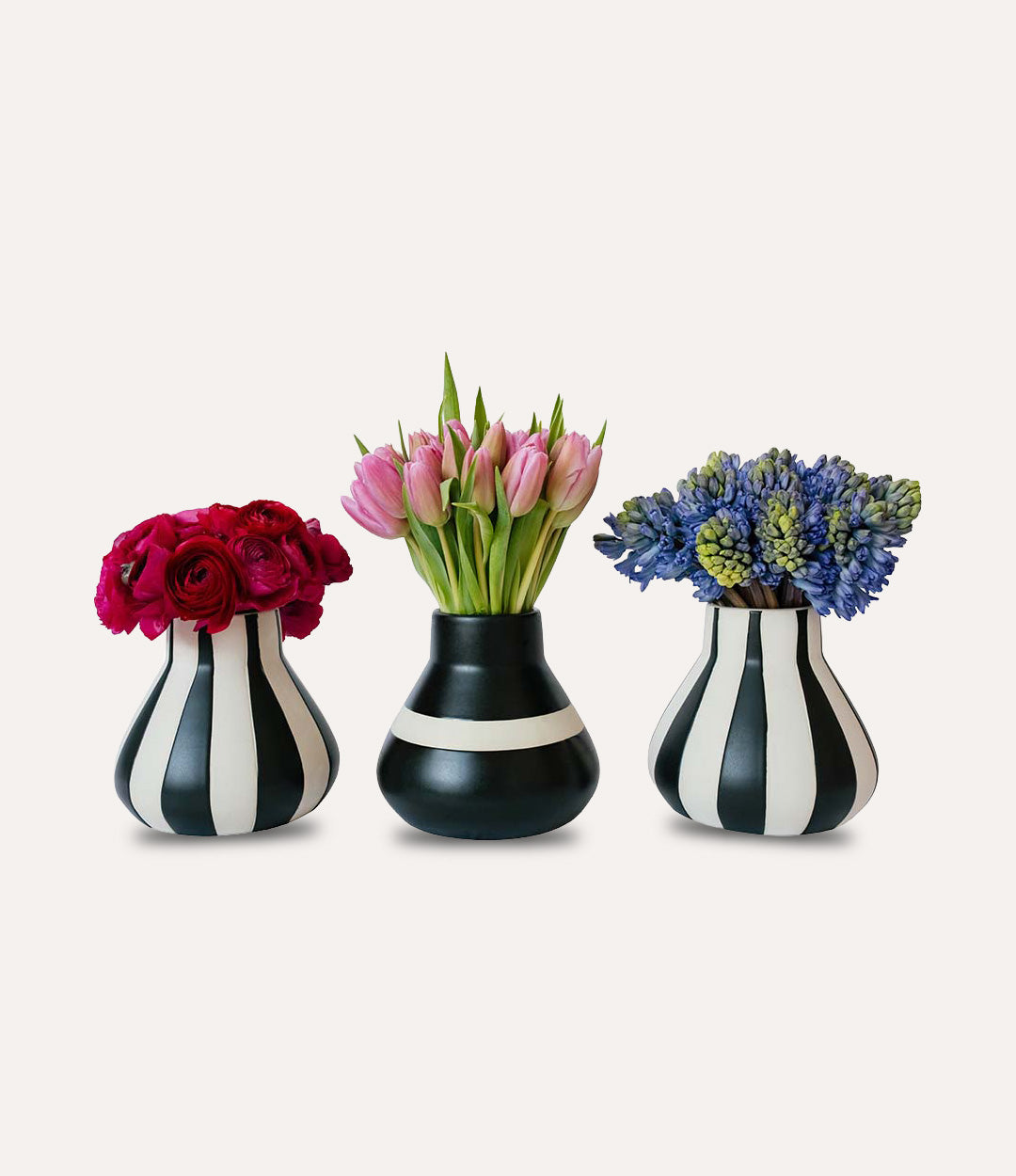 Three black and white striped vases with flowers on a light gray background