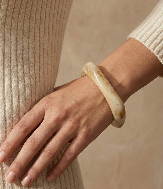 Woman wearing a chunky square bangle made of acrylic and resin in ivory colour displayed on a neutral background.