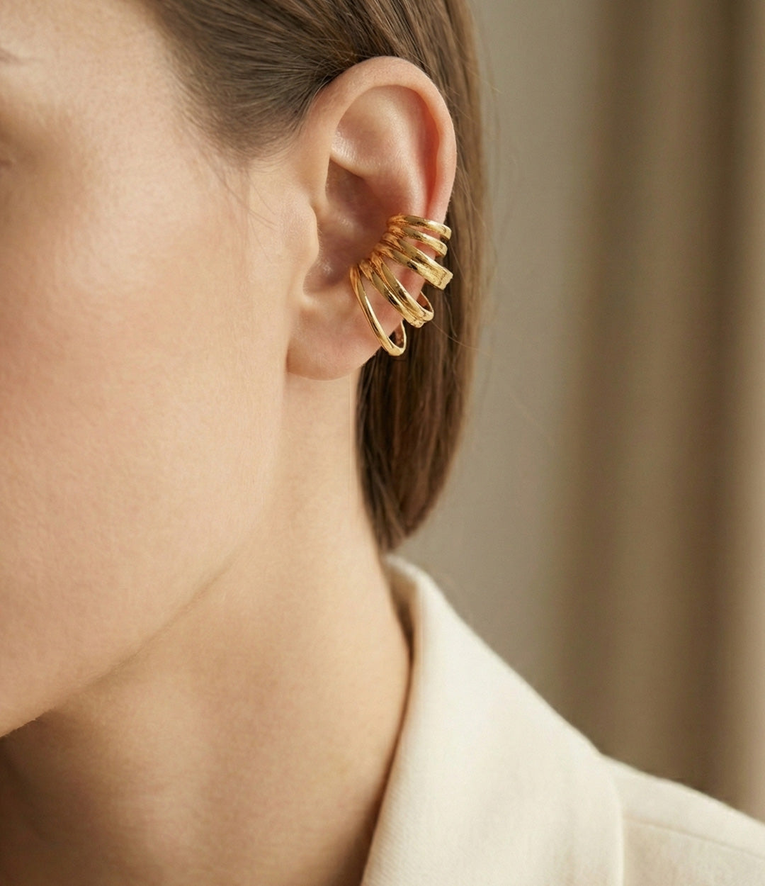 Close-up of a person wearing a gold hoop earring with a neutral background