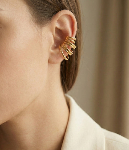 Close-up of a person wearing a gold hoop earring with a neutral background