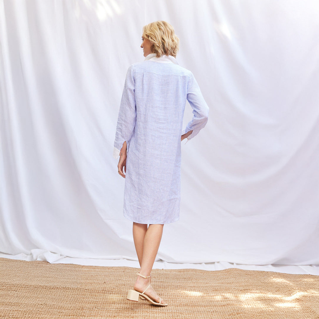 Woman wearing a light blue striped dress against a white curtain background