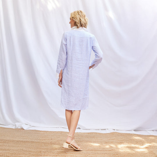 Woman wearing a light blue striped dress against a white curtain background