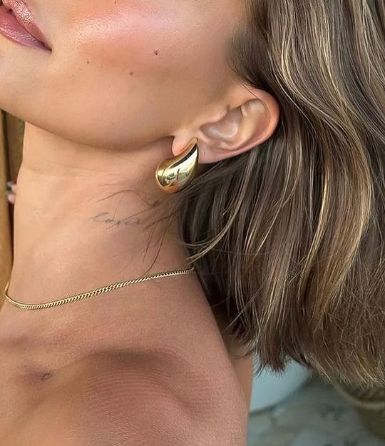 Close up of a model wearing the Tear Drop Stud in gold showing the trendy puffy shape and elegant sculptural fit against a neutral background.