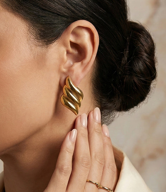 Gold leaf-shaped earring worn by a person with a neutral background