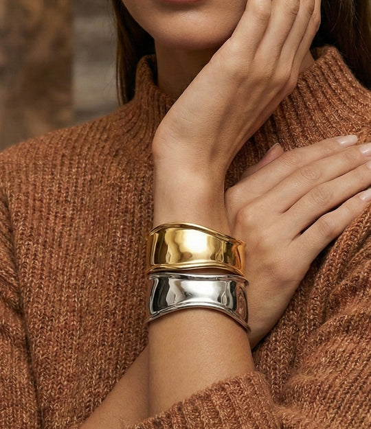 Close-up of a person wearing two gold and silver bracelets on a brown sweater.