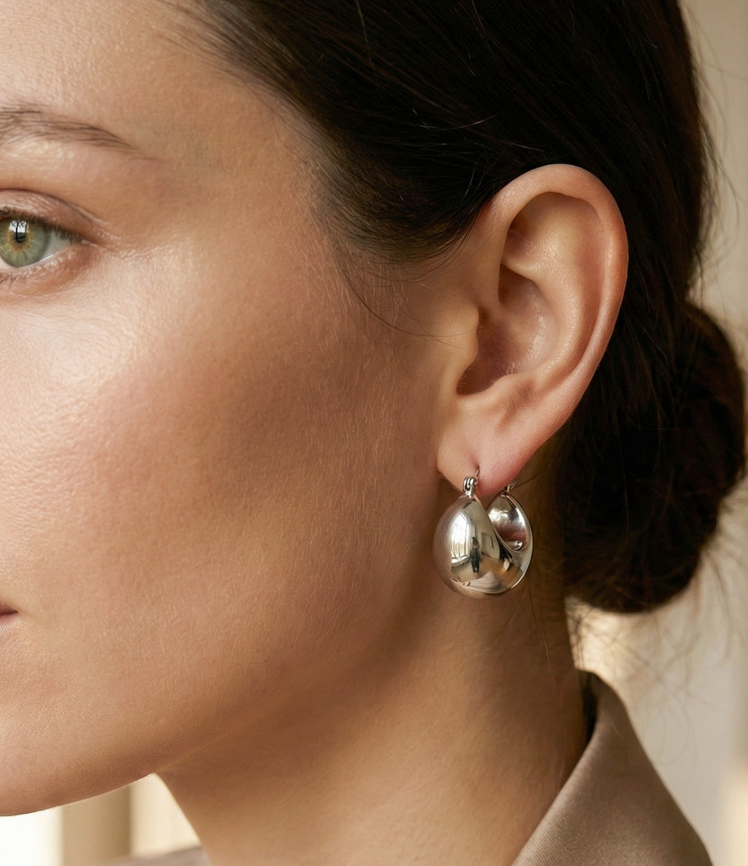 Close-up of a woman wearing silver hoop earrings with a neutral background