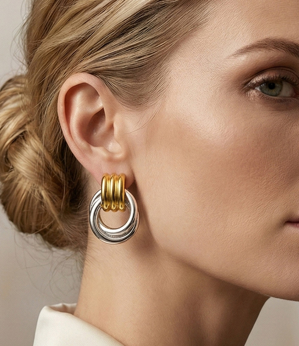 Close-up of a woman wearing gold and silver hoop earrings against a neutral background