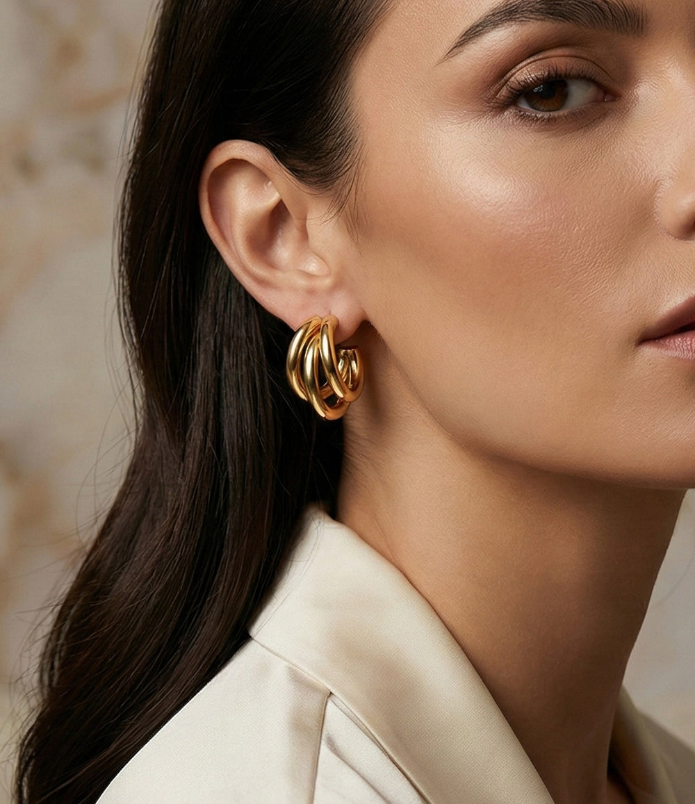 Close-up of a woman wearing gold hoop earrings with a neutral background
