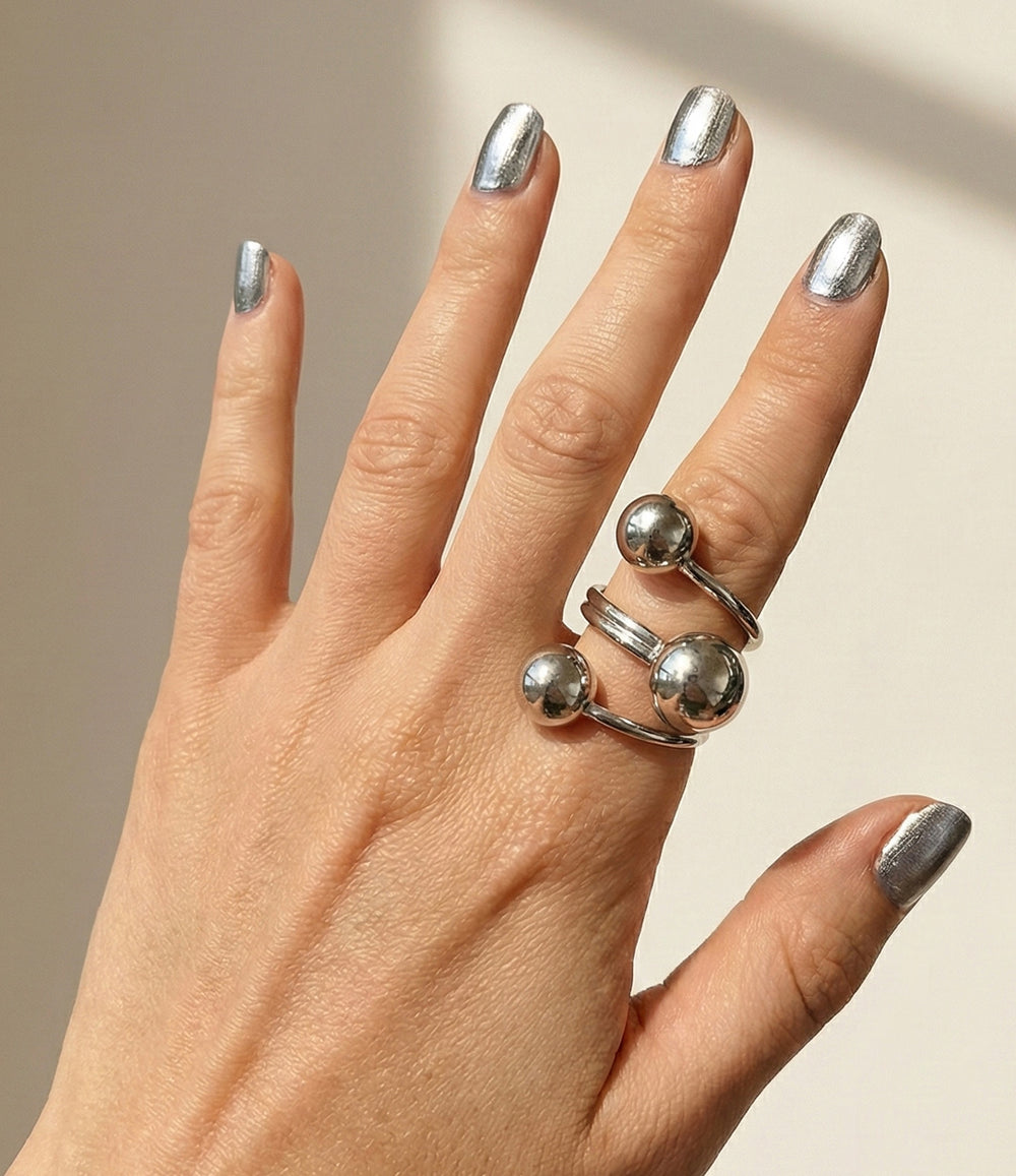 Hand wearing a silver ring with round embellishments on a neutral background