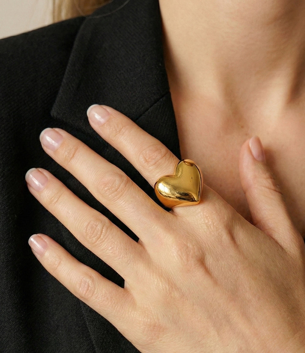Gold heart-shaped ring on a hand with a black blazer background