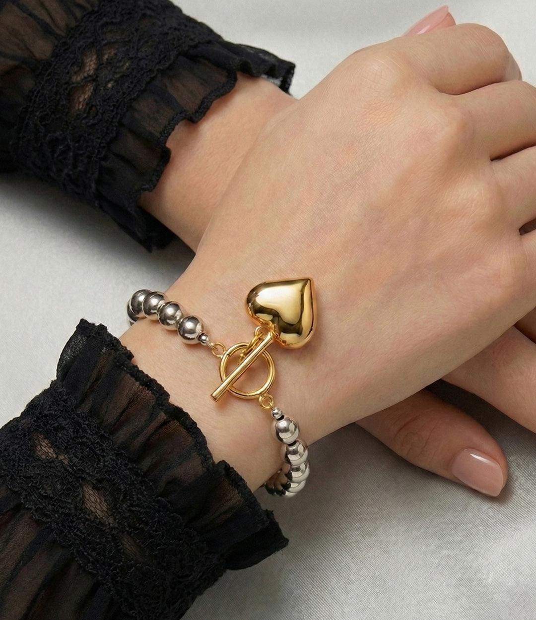 Gold bracelet with a heart-shaped clasp on a wrist against a neutral background
