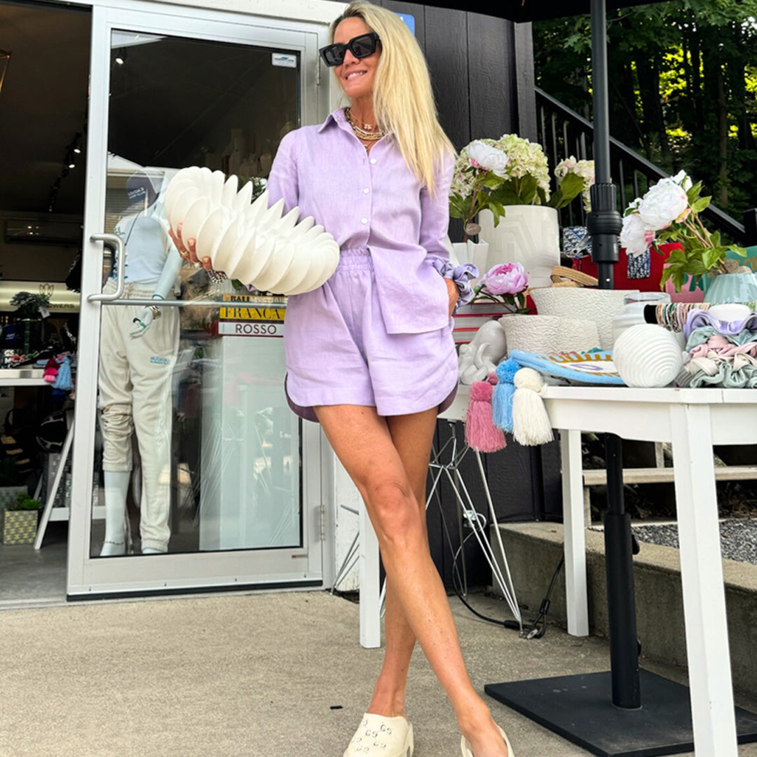 Skye Flowers is in a lavender outfit, holding a large white flower arrangement outdoors.