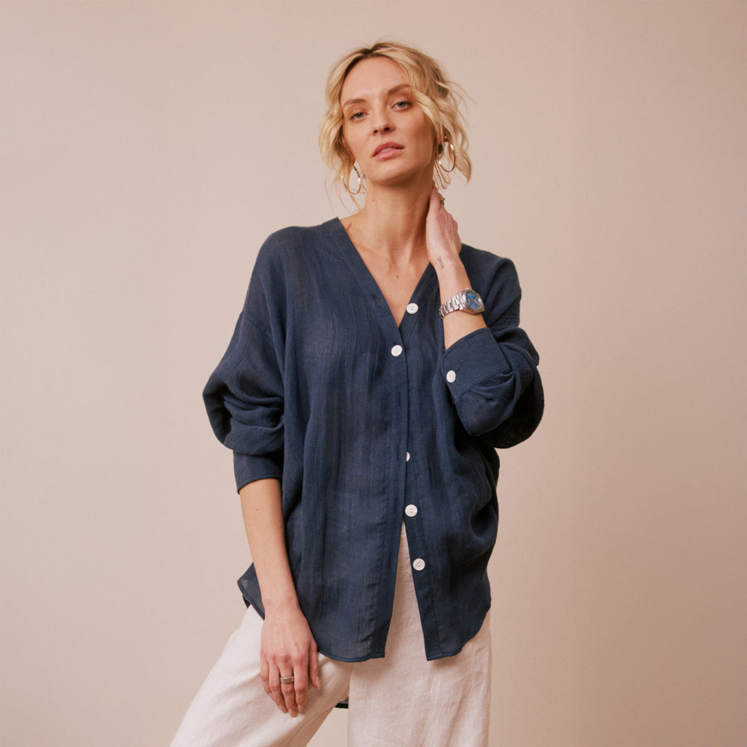 Woman wearing a navy cardigan with white buttons on a beige background