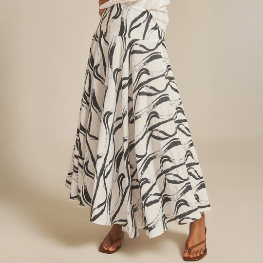 Long white skirt with black abstract pattern worn by a person on a beige background
