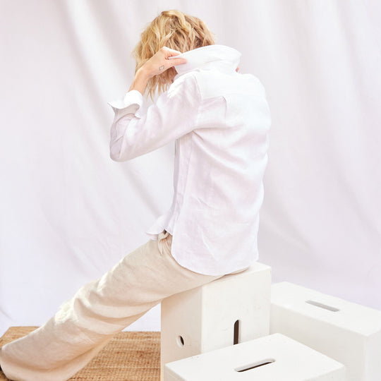 Person wearing a white shirt and beige pants sitting on a white box against a plain background