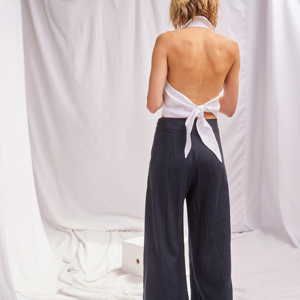 Person wearing a white top with open back and dark pants against a white background