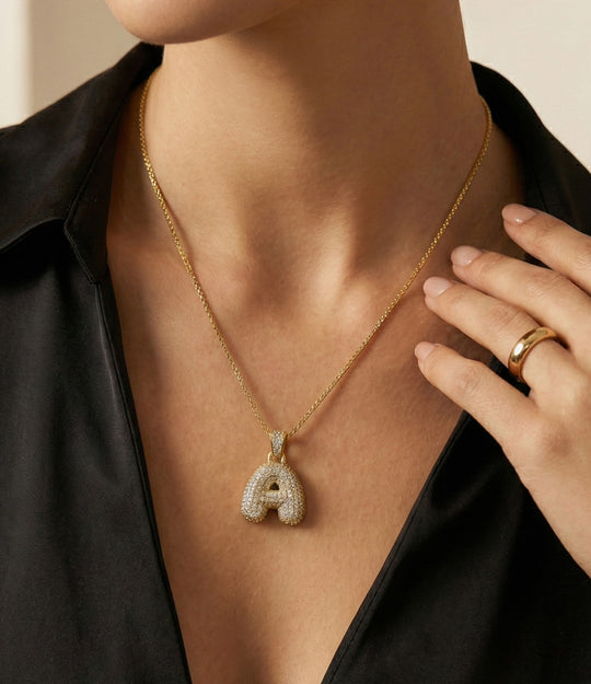 Gold necklace with a letter 'A' pendant worn by a person in a black shirt.