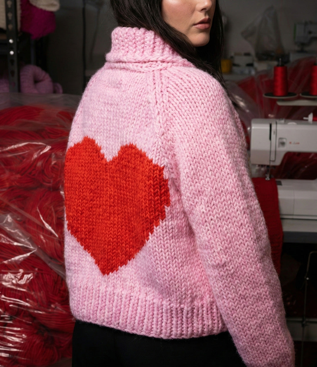Person wearing a pink knitted sweater with a red heart design in a workshop setting.
